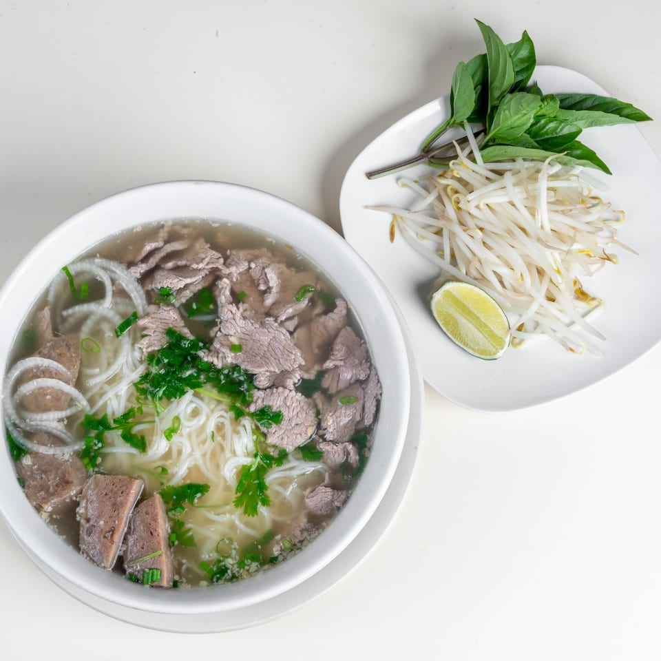 A bowl of Simply Asian Thai Restaurant's pho with beef, noodles, and broth, served with bean sprouts, basil, and lime.