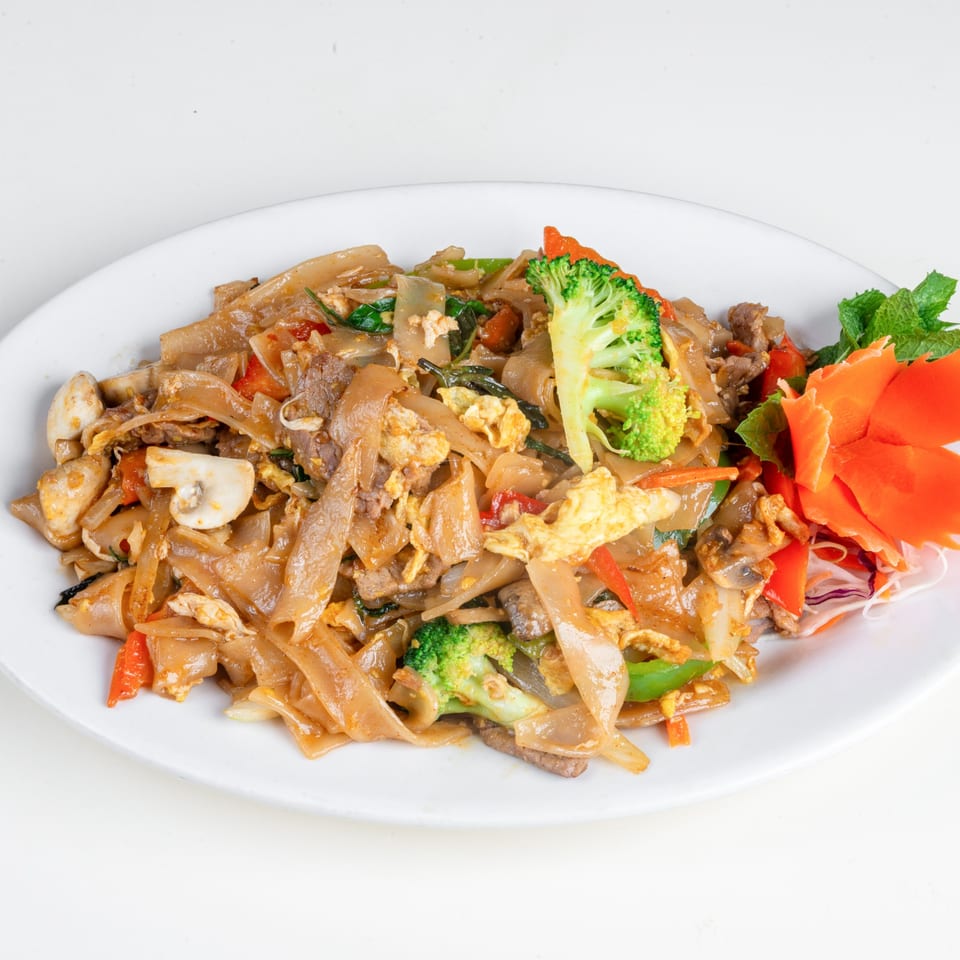 Thai Drunken Noodles with beef, broccoli, mushrooms, and carrots on a white plate.
