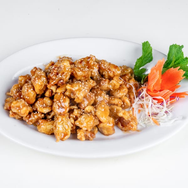 Sesame chicken with a side of shredded carrots, cabbage, and mint on a white plate.