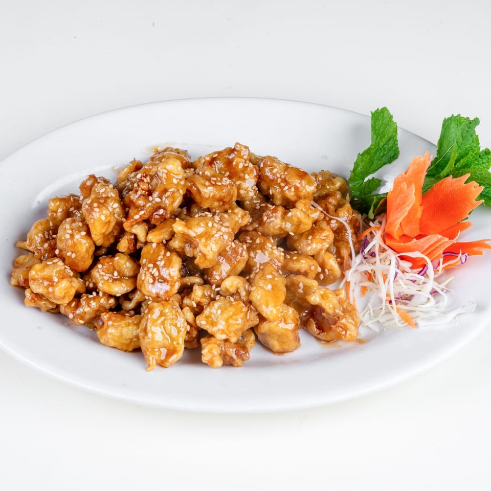 Sesame chicken with a side of shredded carrots, cabbage, and mint on a white plate.