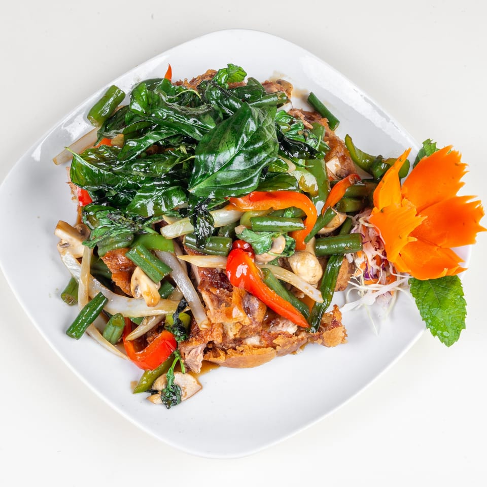 Crispy duck with stir-fried basil, bell peppers, green beans, and mushrooms, garnished with a carrot carving.