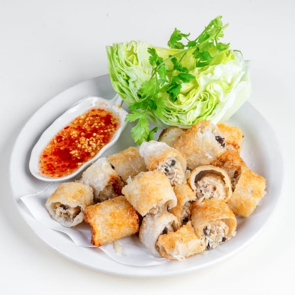 Crispy Thai spring rolls with a sweet chili dipping sauce, lettuce, and cilantro on a white plate.