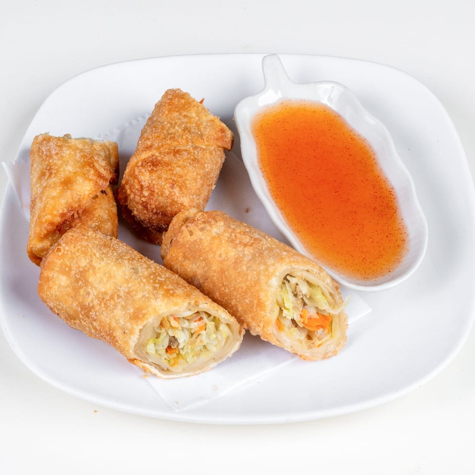 Four crispy Thai spring rolls, two cut open to show vegetable filling, with a side of sweet chili sauce.