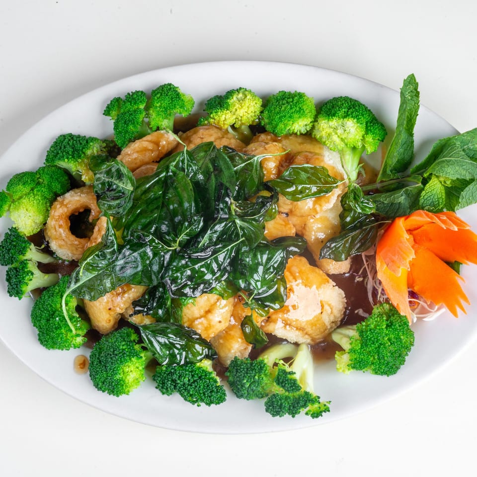 Thai basil chicken with broccoli, carved carrots, and mint on a white plate.