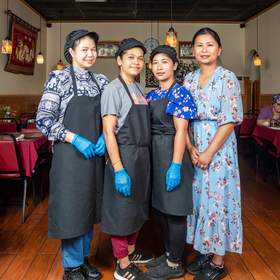 Four Simply Asian Thai Restaurant staff members, three in aprons and gloves, stand in the dining room.