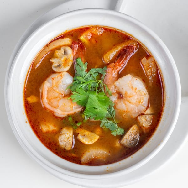 Close-up of a vibrant Thai Tom Yum soup with shrimp, mushrooms, and cilantro in a white bowl.