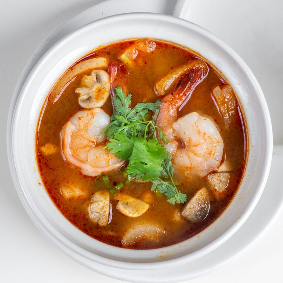 Close-up of a vibrant Thai Tom Yum soup with shrimp, mushrooms, and cilantro in a white bowl.