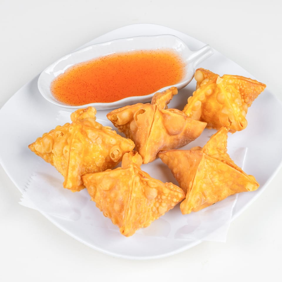 Crispy golden fried wontons arranged on a white plate with a side of sweet chili dipping sauce.