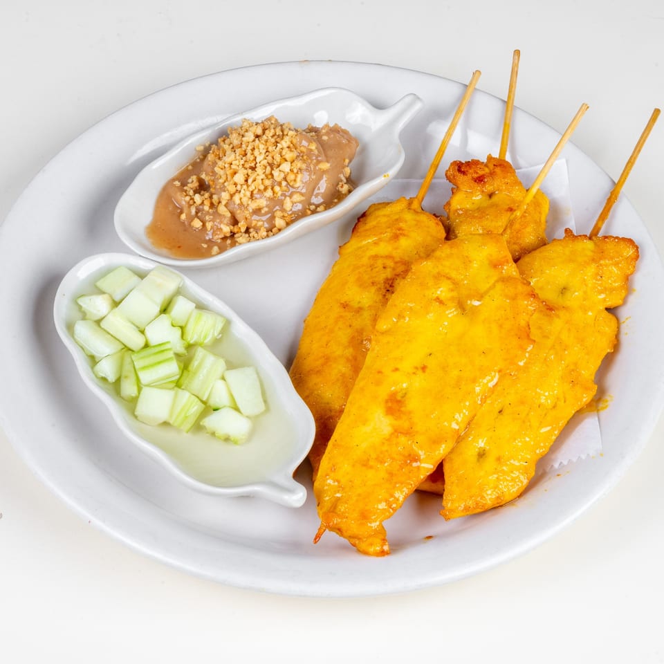 Simply Asian Thai Restaurant's chicken satay skewers with peanut sauce and cucumber salad on a white plate.