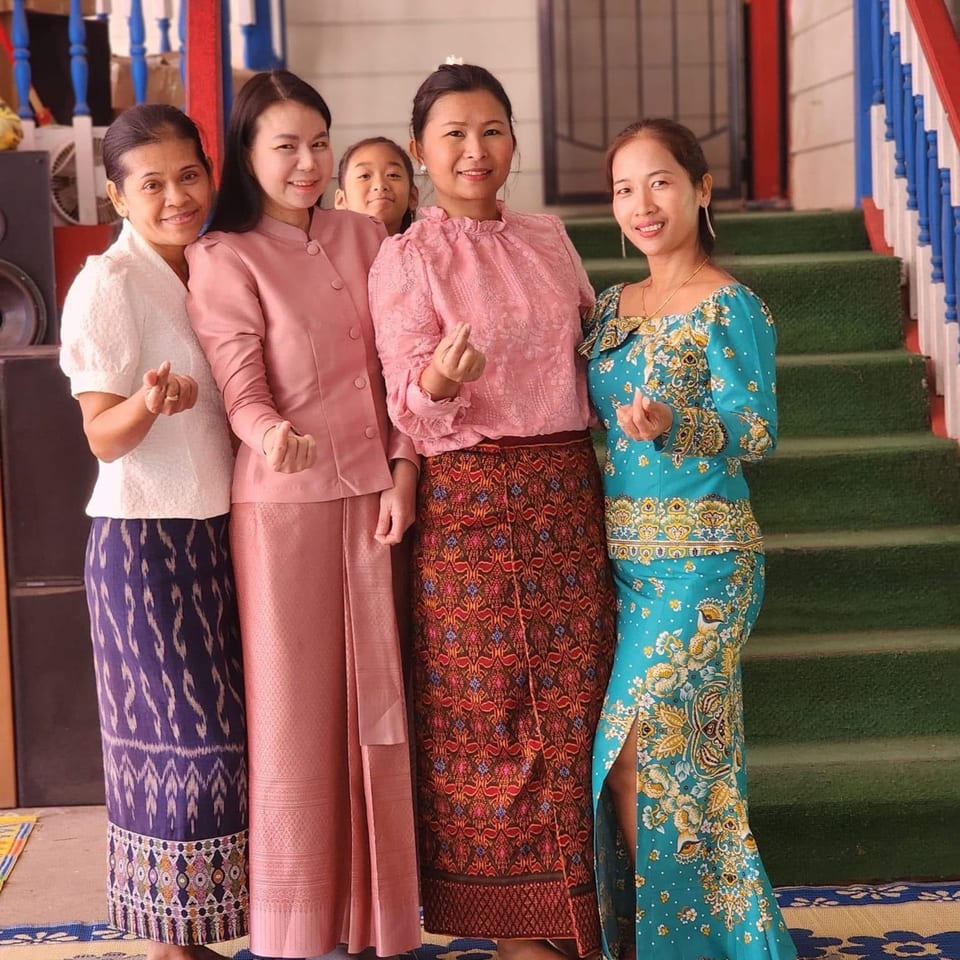 Four Thai women and a child in traditional dresses pose, smiling, with a green staircase in the background.