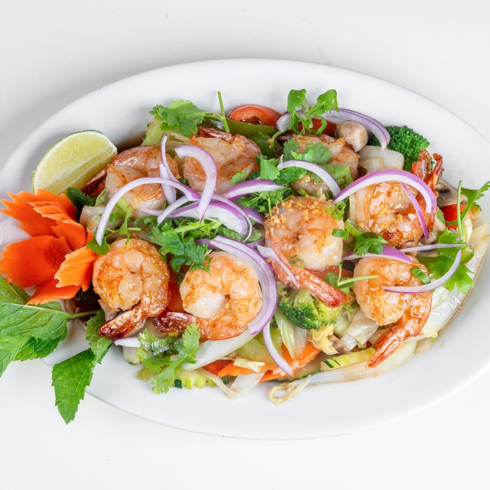 Thai shrimp salad with red onions, cilantro, lime, and carved carrots on a white plate.
