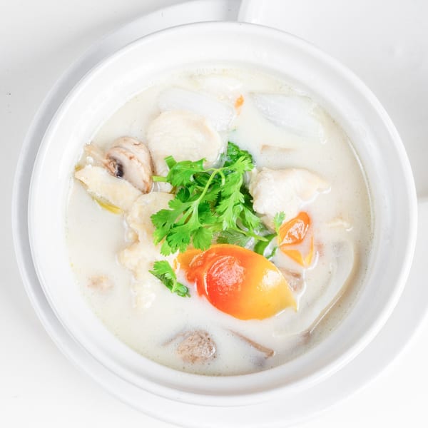 Creamy Thai coconut soup with chicken, mushrooms, tomatoes, and cilantro in a white bowl.